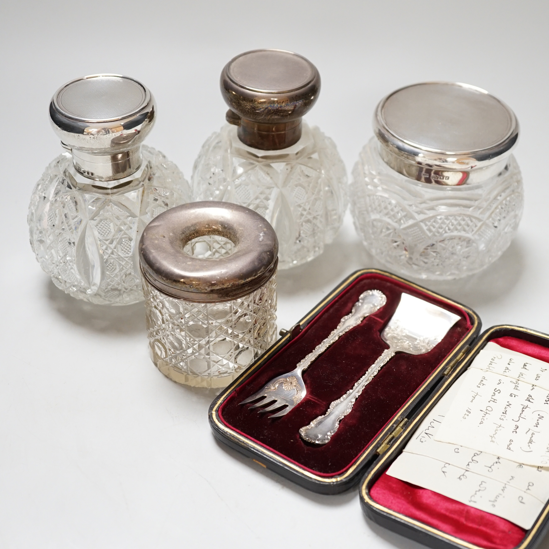 A pair of George V silver mounted cut glass scent bottles, London 1920, 11cm, a similar toilet jar, a hair tidy and a cased two piece christening set